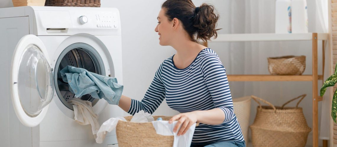 Beautiful young woman is smiling while doing laundry at home.